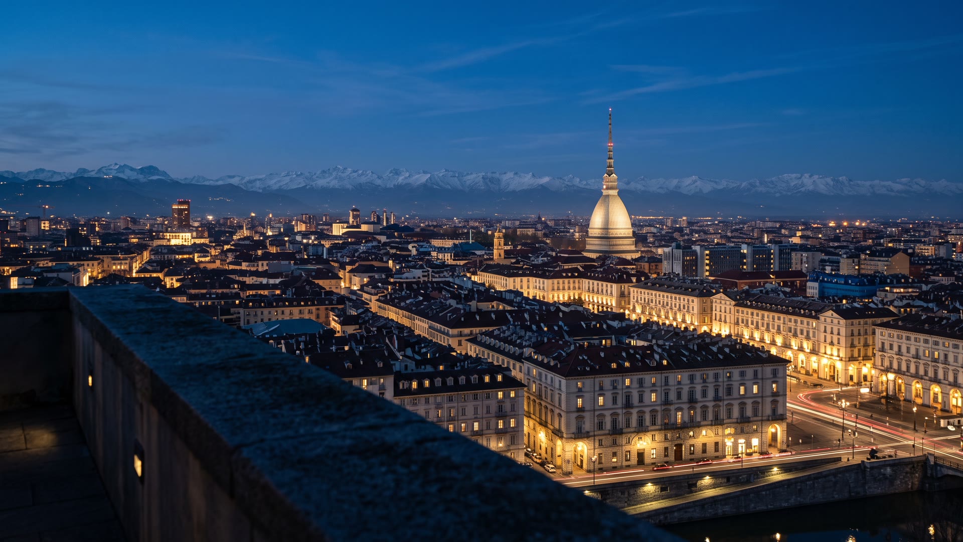 Torino all'ora blu da una terrazza del centro, con la Mole Antonelliana illuminata e le Alpi innevate