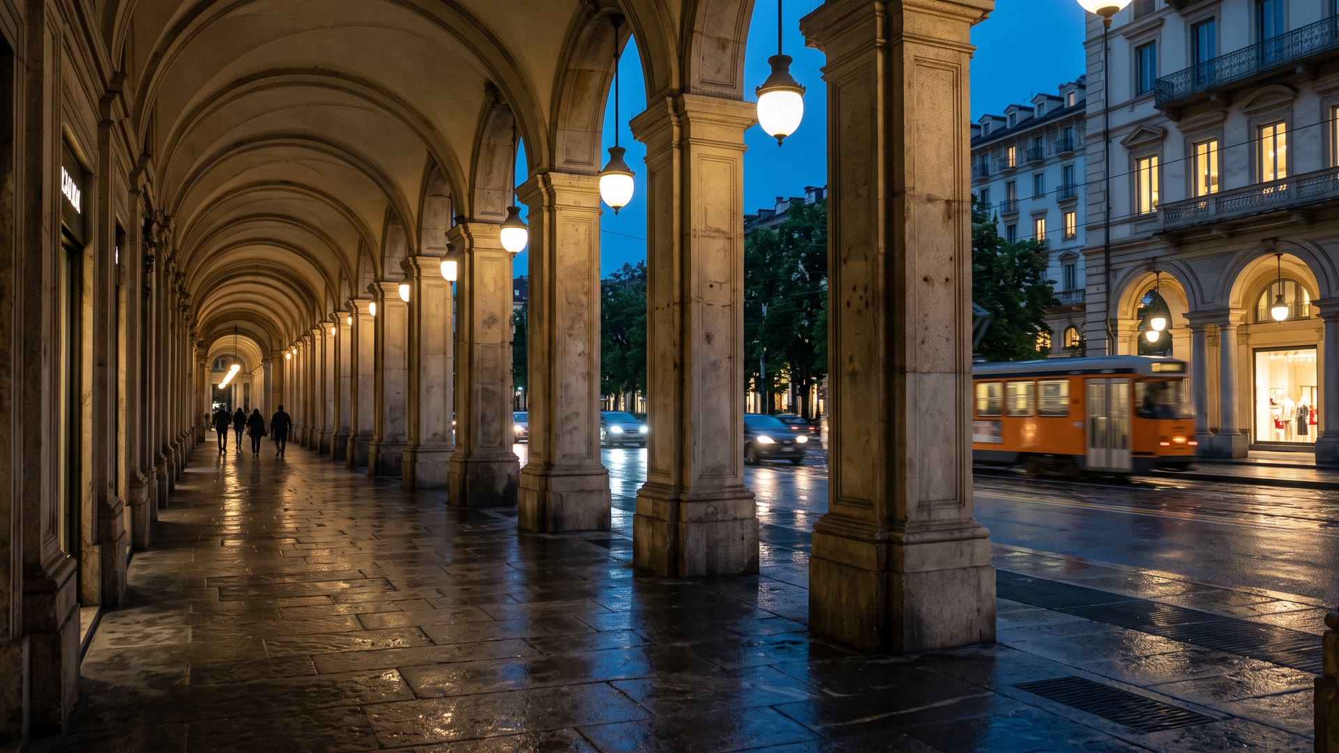 I portici del centro di Torino all'ora blu, con i lampioni accesi, le vetrine e un tram di passaggio