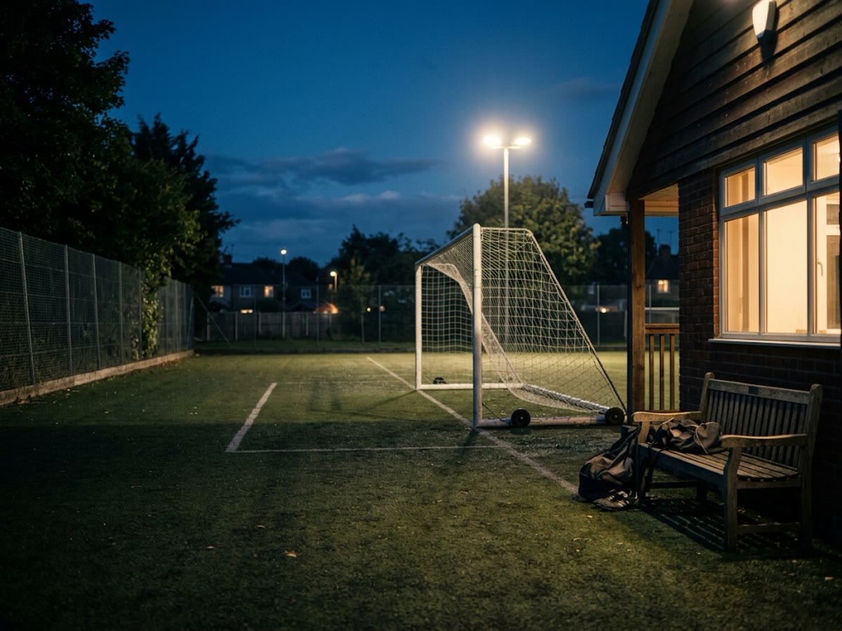 Campo di calcio di quartiere all'ora blu sotto i riflettori con panchina e club house illuminata